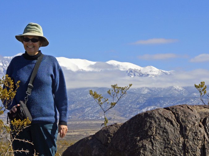 Peggy stands on the ridge next to a rock likely to hold petroglyphs. Some glyphs are immediately obvious while others are hidden. Sharp eyes are required.