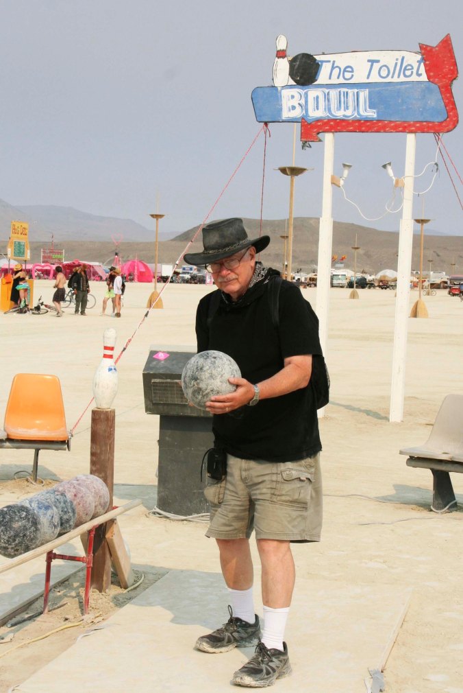 Colorful signs announced the presence of some port-a-potties on the Playa. This one was named the Toilet Bowl and came with a bowling alley. Here I line up to take a shot. I managed to knock down all but one pin. (photo by Peggy Mekemson)
