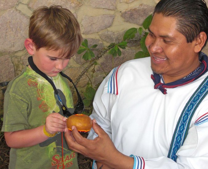 Ernesto shows lets our grandson Cody press beads onto a gourd covered with beeswax. (Photo by Ethan's mom, Natasha.)