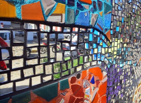 Made with tile and glass, the mural uses mirrors to reflect the street scene behind it, an effort that adds both beauty and interest.