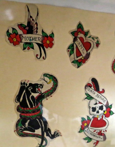 The walls of Triangle Tattoo in Fort Brag are covered with traditional tattoo art. I would have to be drunk, knocked out, and tied down to have a tattoo of a skull or Mother scratched on my body.