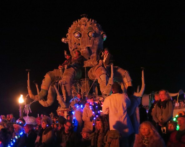 People perch on El Pulpo Mechanico at Burning Man and watch as the Man burns.