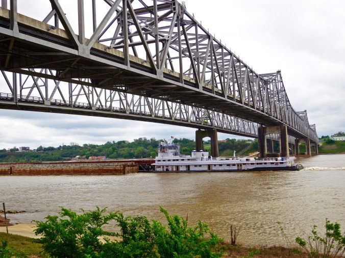 A side view of the Visalia-Natchez Bridge across the Mississippi River with a barge passing under it.
