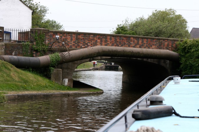 Piloting narrowboat under bridge on Trent and Mercy Canal